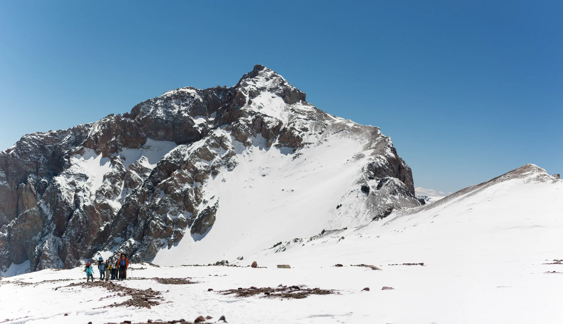 Climbers moving below Aconcagua's snow-covered upper mountain.